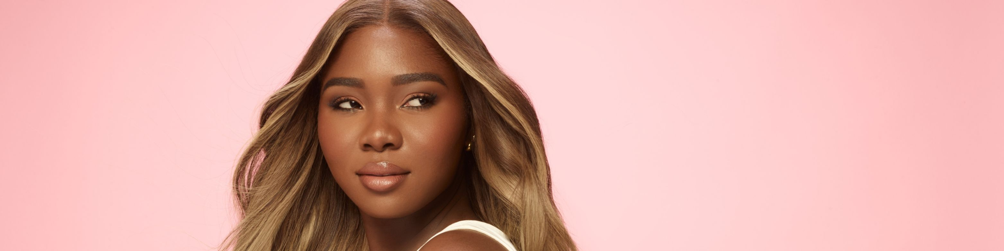 A close up face view of a beautiful woman in a ash blonde wig on a pink background.
